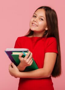 smiling schoolgirl holding books and looking camera
