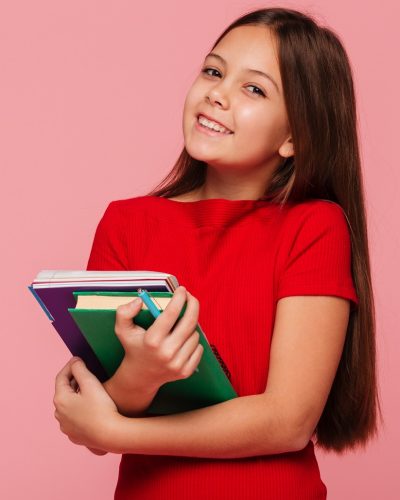 smiling schoolgirl holding books and looking camera